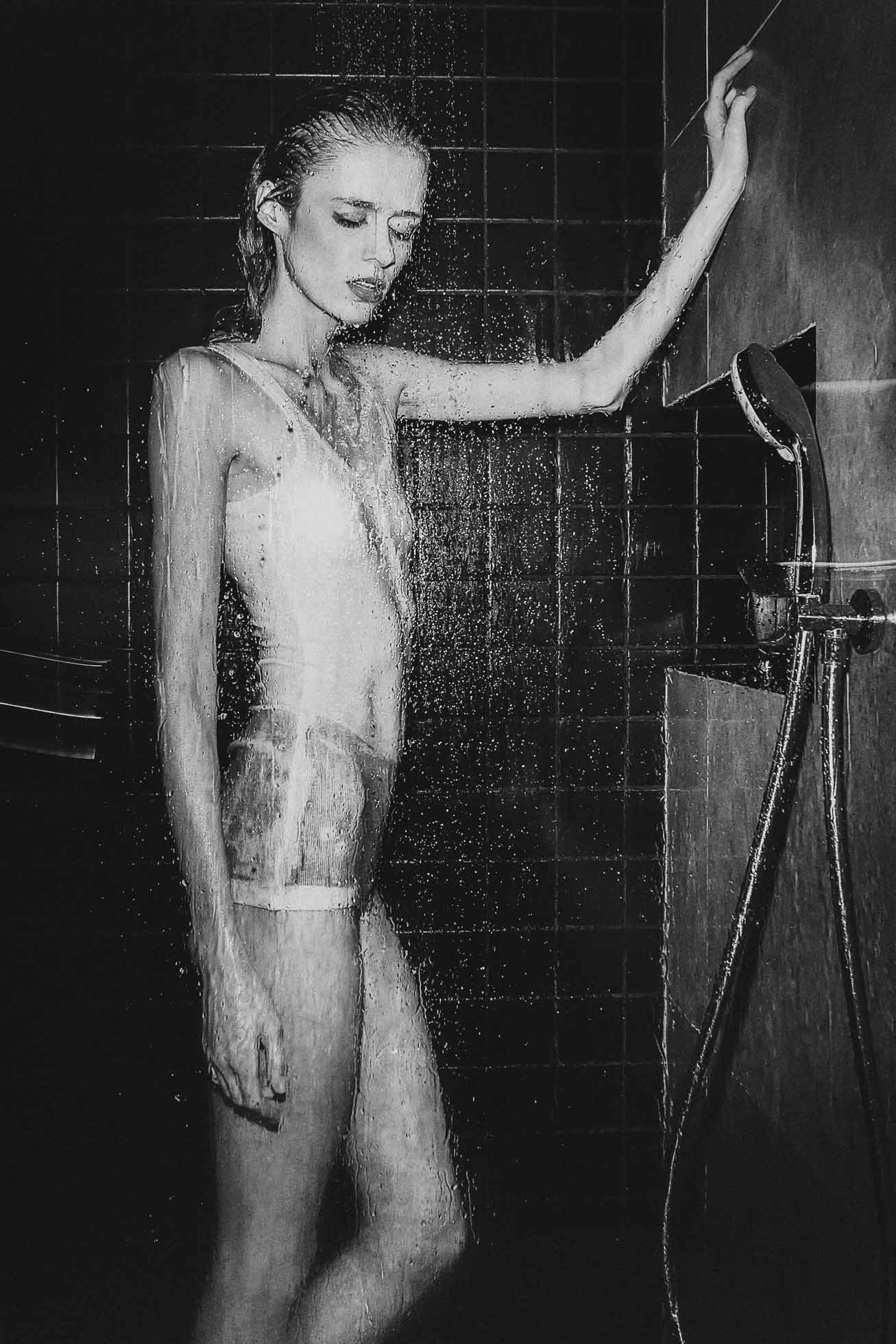 Osoba stojąca pod prysznicem w kostiumie kąpielowym, po której spływa woda. Kafelkowana część prysznica tworzy scenę w czerni i bieli, podkreślając kontrast kropel na tle. Ta uderzająca chwila uchwyca istotę fotografii edytorialowej Trójmiasto.