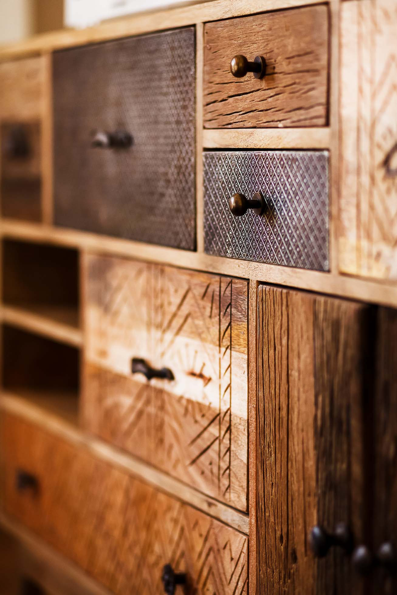 Zbliżenie na eklektyczną drewnianą komodę o różnych fakturach i wykończeniach. Szuflady, idealne na sesje fotograficzne wnętrz Gdańsk,Gdynia,Sopot – usługi fotograficzne, mają różne rozmiary i wzory, z mieszanymi gałkami i uchwytami, tworząc rustykalną i rzemieślniczą estetykę.